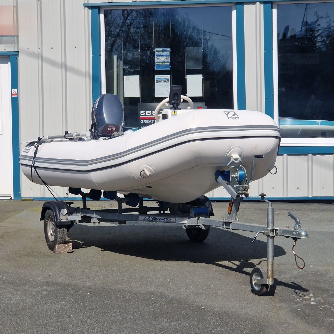 Inflatable boat on a trailer in front of a building with large windows.