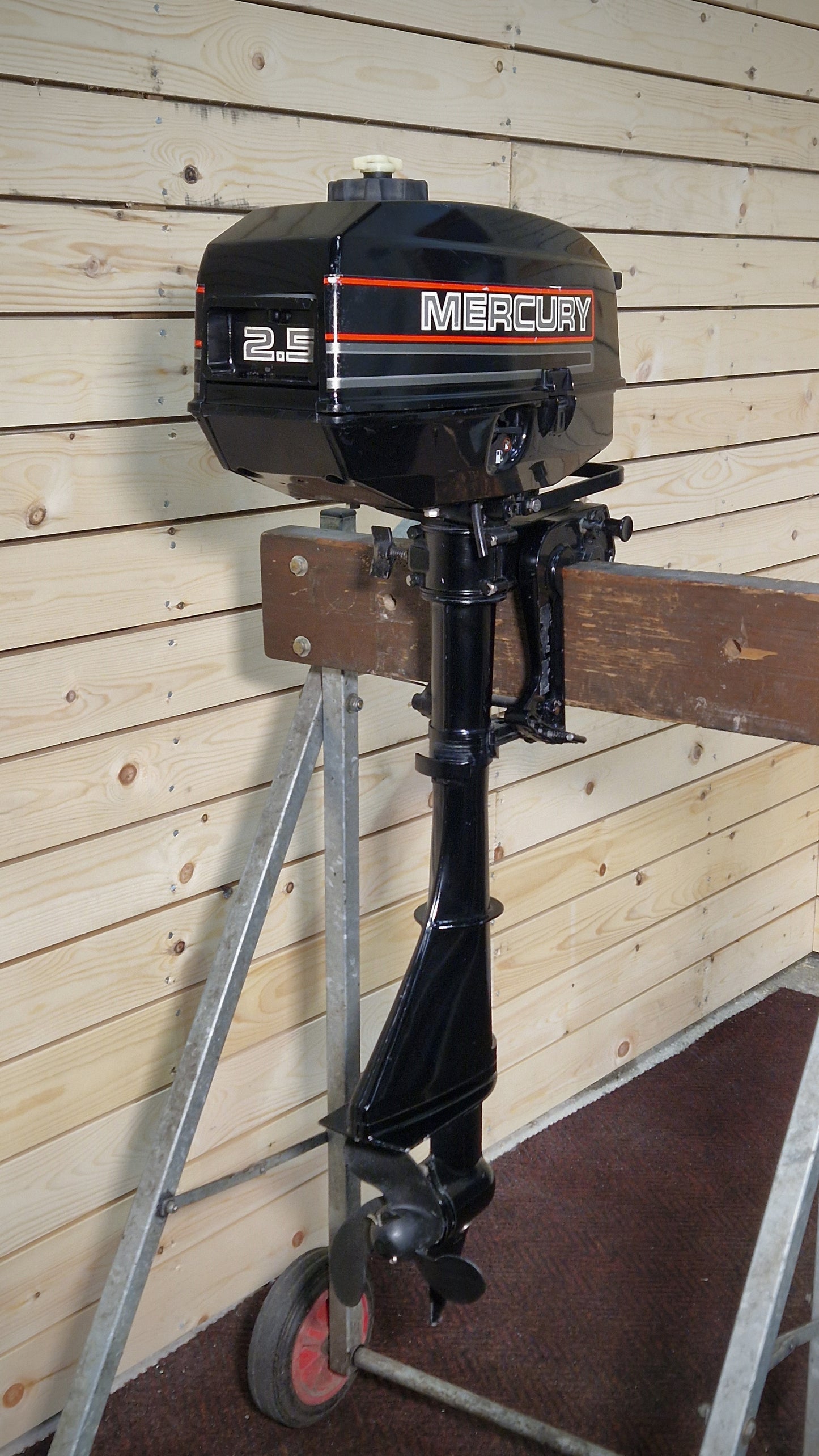 Black Mercury outboard motor on a stand against a wooden wall.