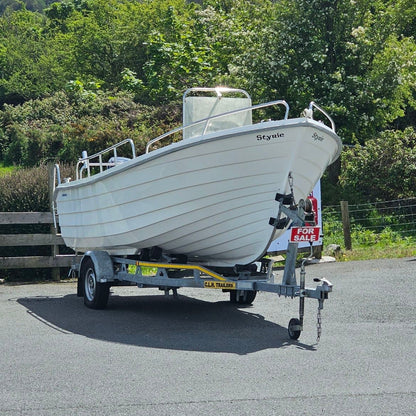 White boat on a trailer in a parking lot with greenery in the background