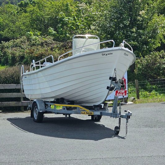 White boat on a trailer in a parking lot with greenery in the background